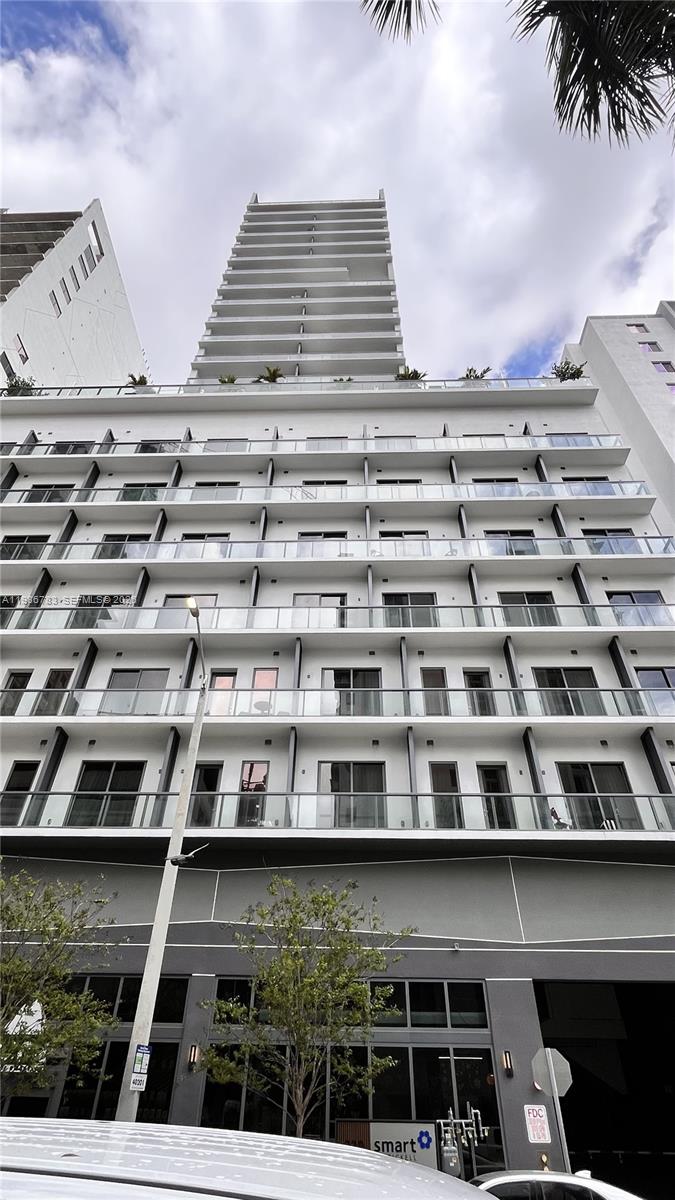 A low-angle exterior view of a modern high-rise apartment building with multiple glass-railed balconies — 229 SW 9th St # 307, Miami FL 33130, MIAMI, FL