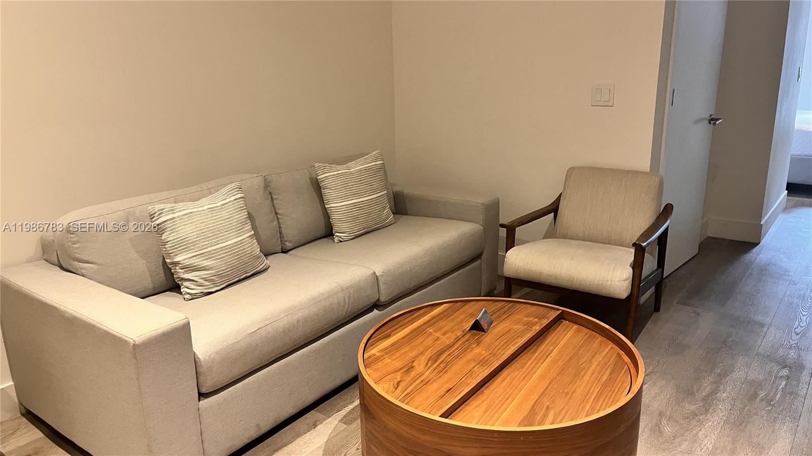 A living room features a gray sofa, a wooden armchair, and a round wooden coffee table — 229 SW 9th St # 307, Miami FL 33130, MIAMI, FL