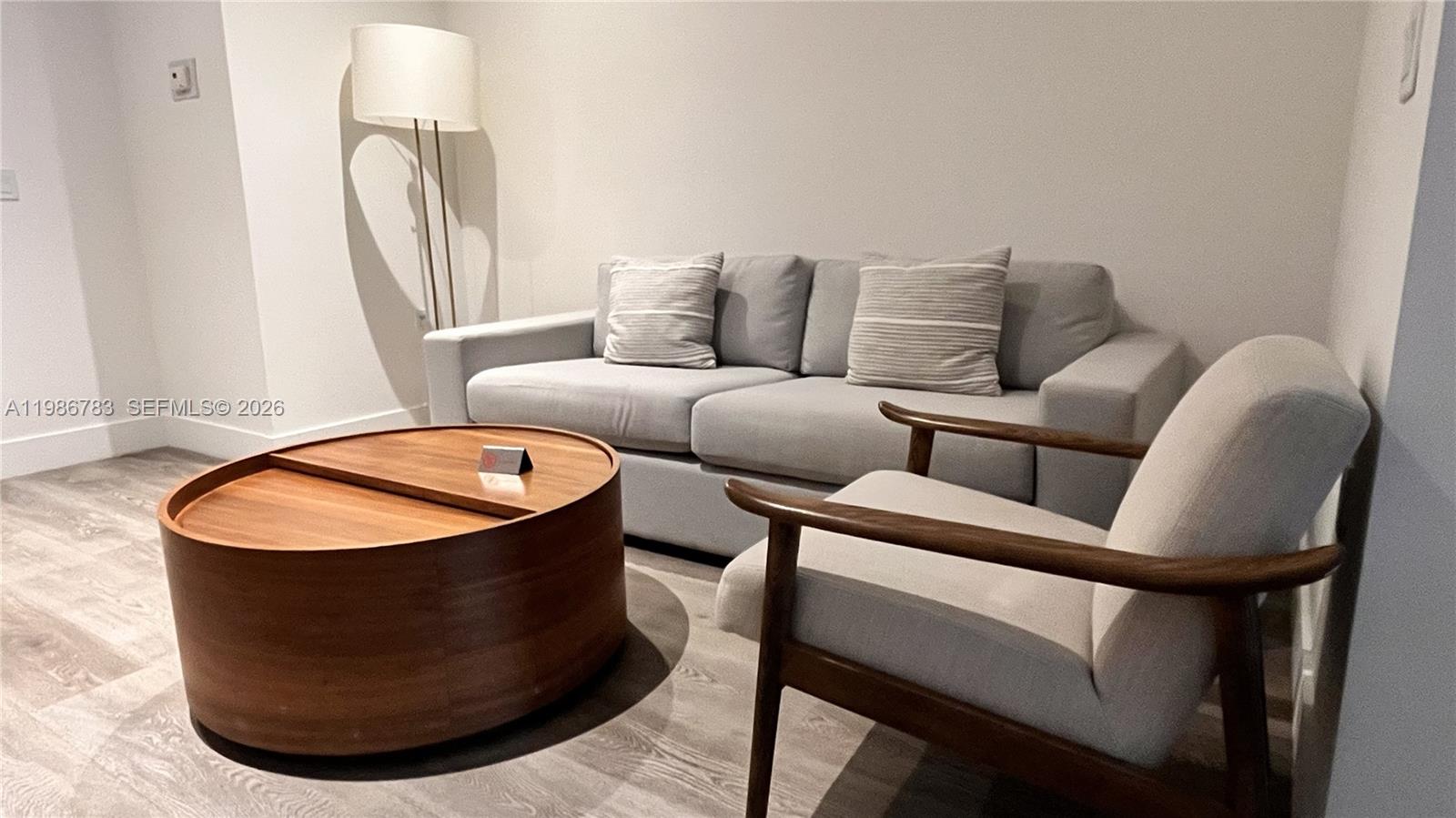 A living room features a light gray sofa, a wooden armchair, and a round coffee table — 229 SW 9th St # 307, Miami FL 33130, MIAMI, FL