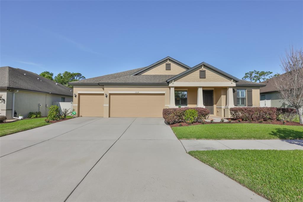 A single-story suburban house with a three-car garage, tan stucco siding, and a concrete driveway — 11014 BRAHMAN RANCH CIRCLE, RIVERVIEW, FL