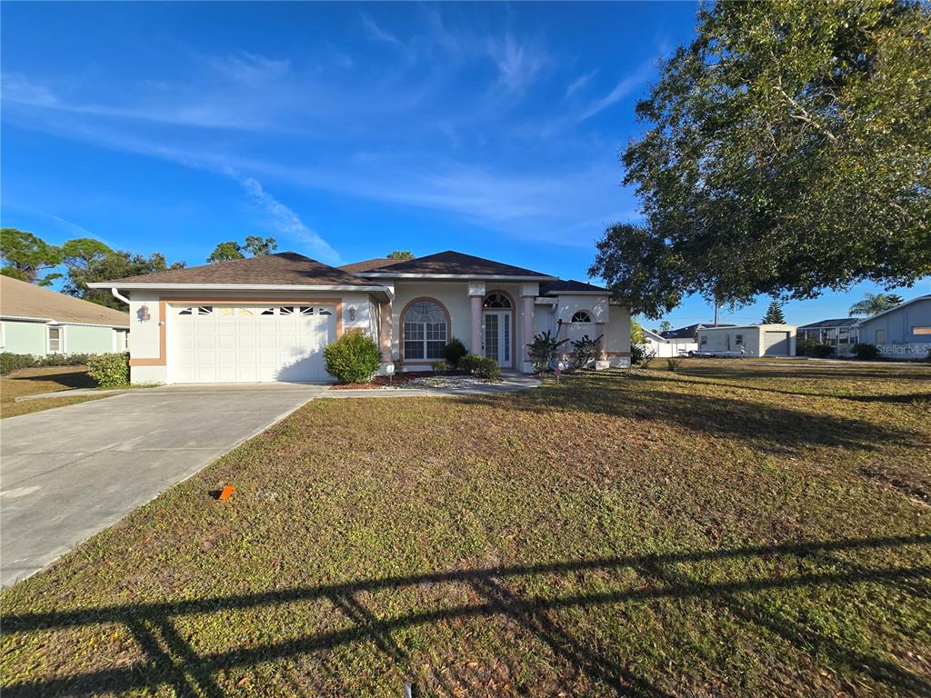 A single-story house with a white garage, arched window, and a large front lawn — 23404 PEACHLAND BOULEVARD, PORT CHARLOTTE, FL