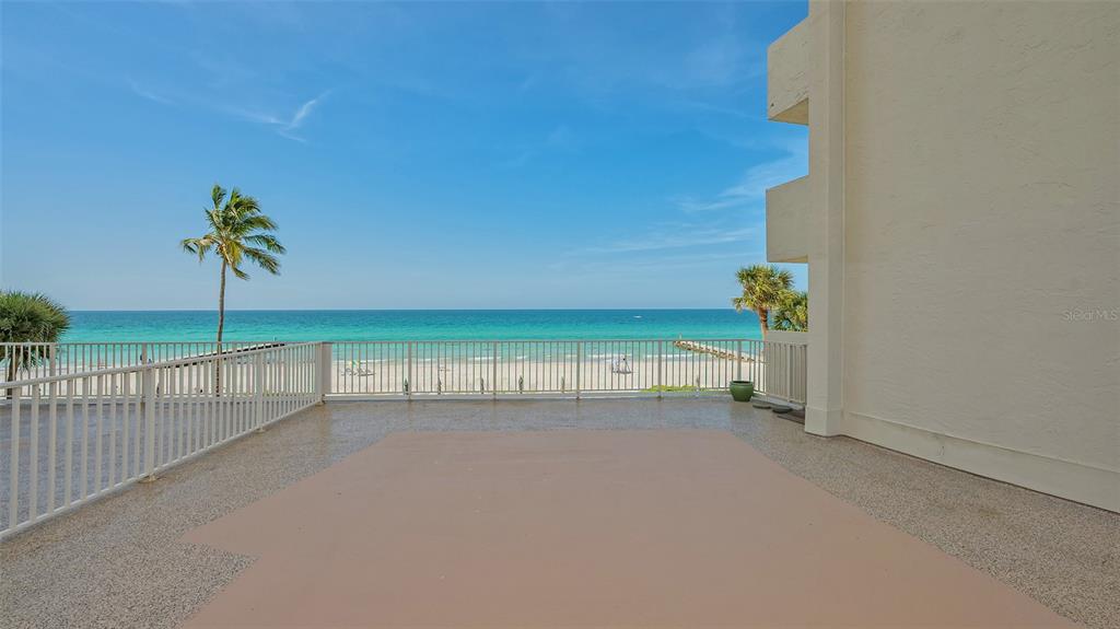 A spacious outdoor balcony overlooks a sandy beach and the ocean under a blue sky — 2301 GULF OF MEXICO DRIVE UNIT 33N, LONGBOAT KEY, FL