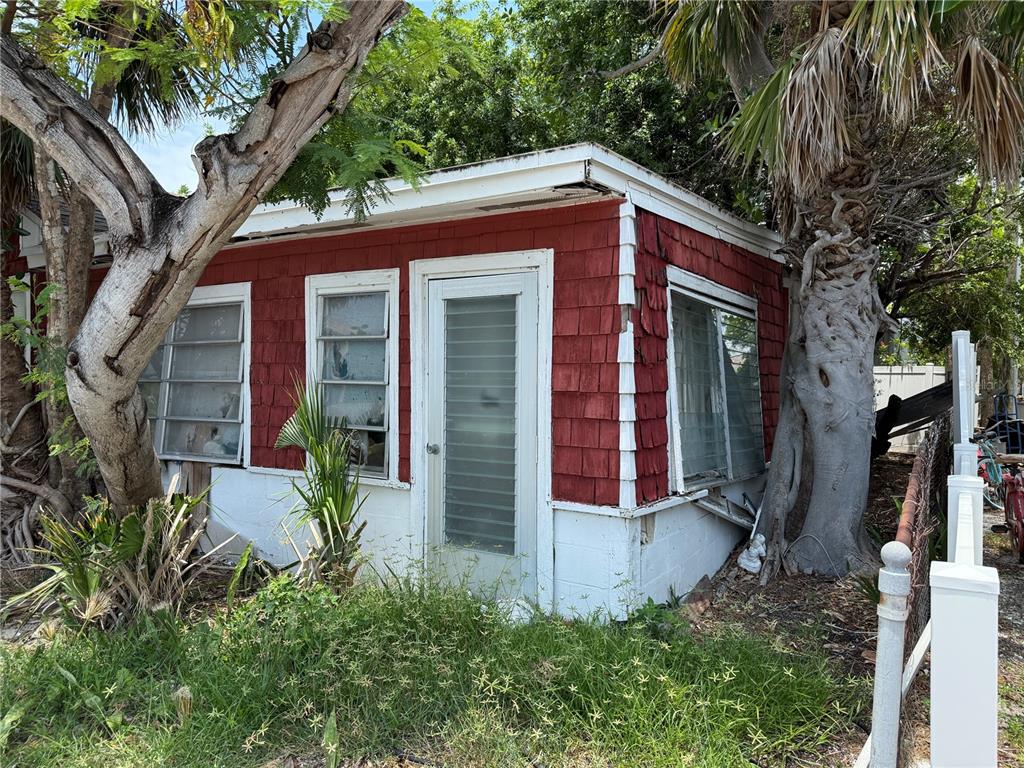 A small, red-shingled exterior structure with white trim, louvered windows, and a glass-paneled door — 116 85TH AVENUE, TREASURE ISLAND, FL