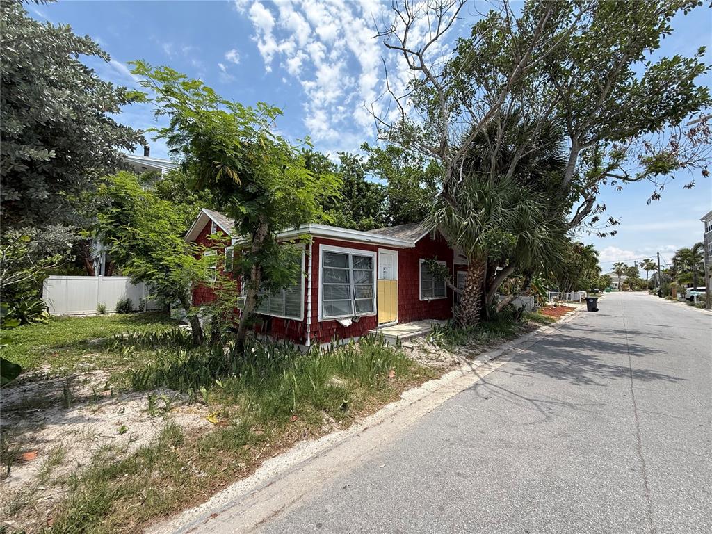 A red, single-story house with white trim sits on a sandy lot beside a street — 116 85TH AVENUE, TREASURE ISLAND, FL