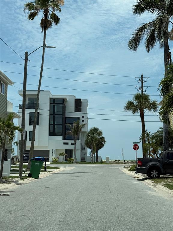 A modern white multi-story house stands at the end of a paved residential street — 116 85TH AVENUE, TREASURE ISLAND, FL