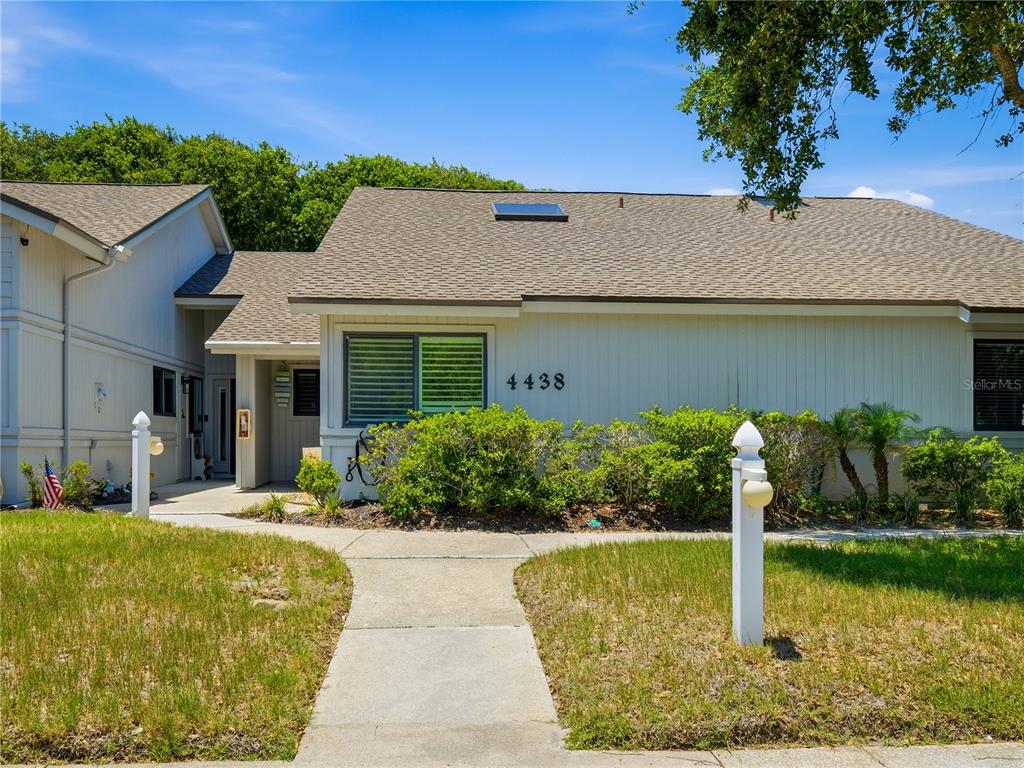 A light-colored single-story house features a shingled roof, a concrete walkway, and green landscaping — 4438 SEA MIST DRIVE UNIT 4438, NEW SMYRNA BEACH, FL