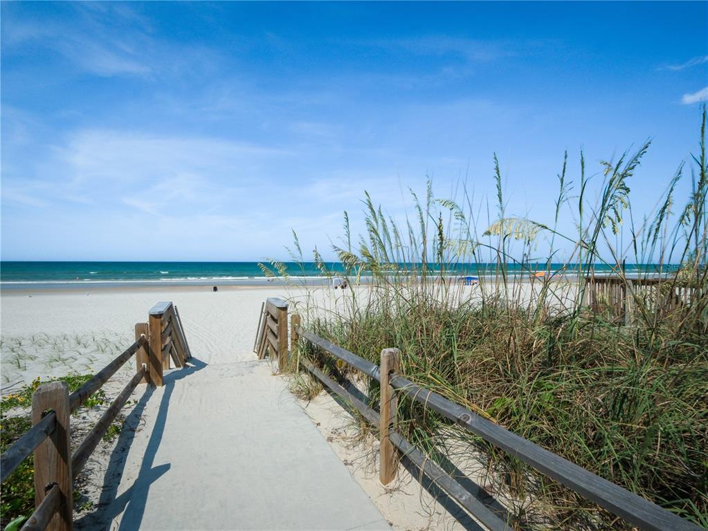 A concrete walkway leads through a wooden fence and sand dunes toward the ocean beach — 4438 SEA MIST DRIVE UNIT 4438, NEW SMYRNA BEACH, FL