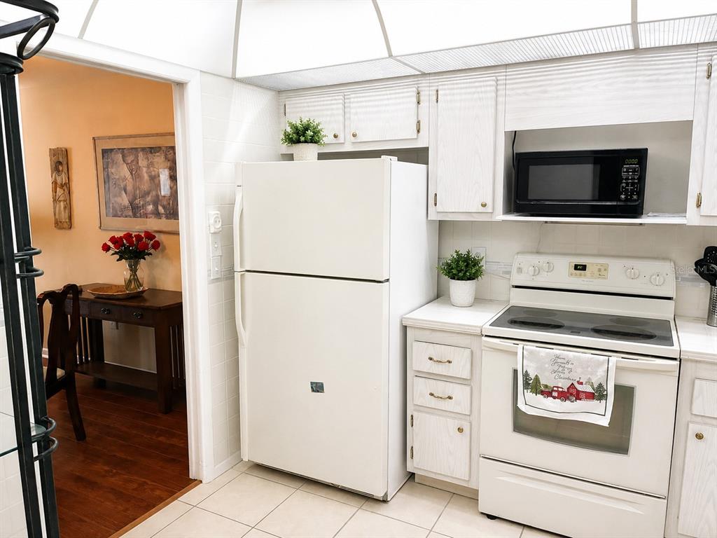 A kitchen with white cabinets, white appliances, and a doorway leading to a dining area — 4575 COVE CIRCLE UNIT 506, ST PETERSBURG, FL