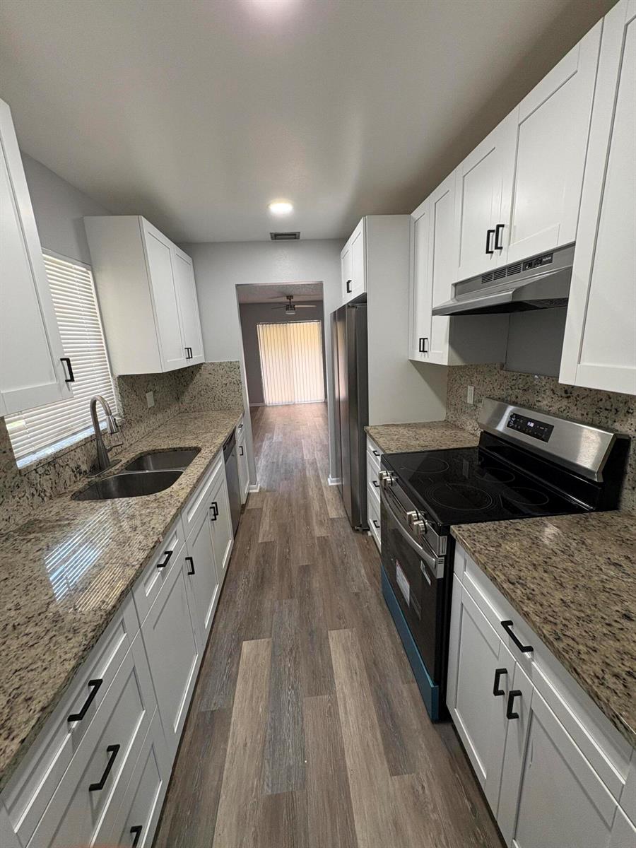 A galley kitchen features white cabinets, granite countertops, stainless steel appliances, and wood-look flooring — 4726 Summit Boulevard, West Palm Beach FL 33415, WEST PALM BEACH, FL
