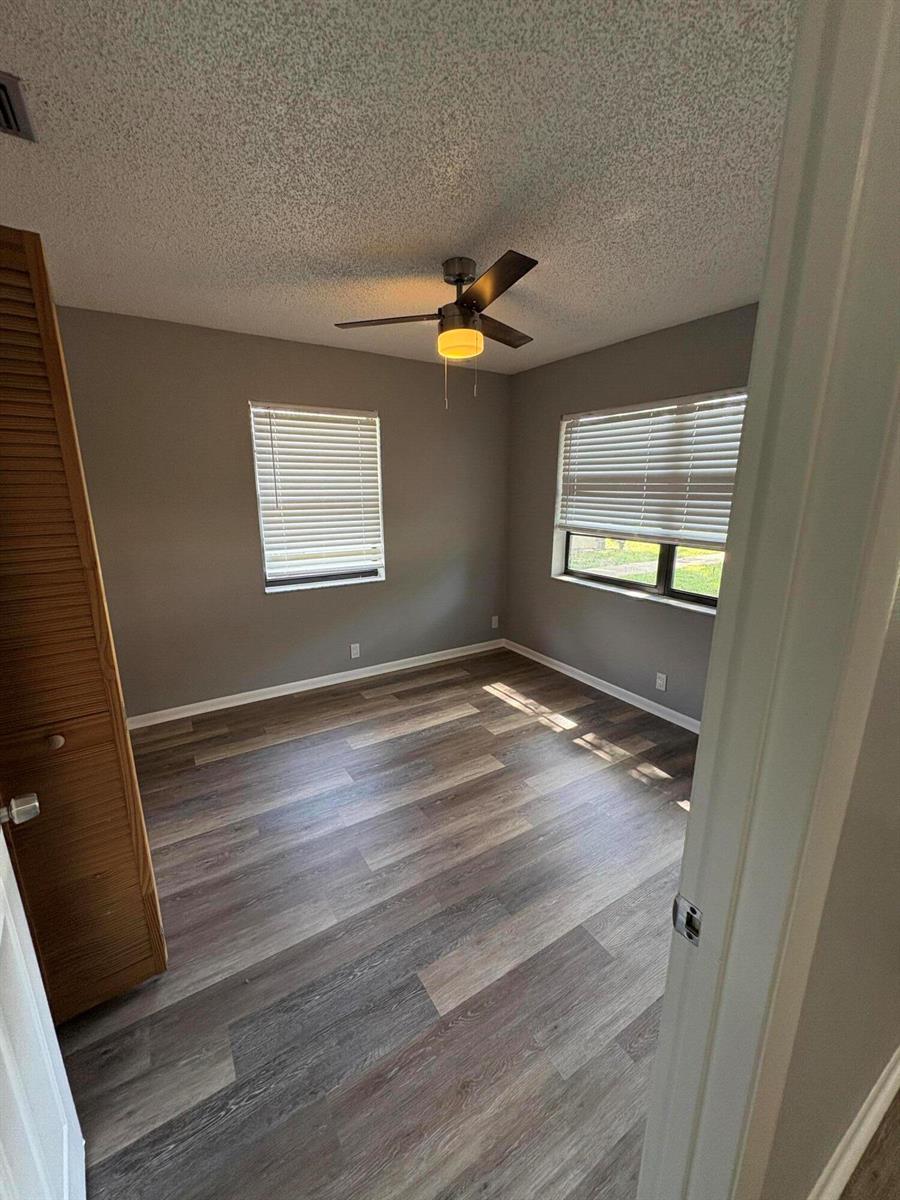 An empty bedroom features gray walls, wood-look flooring, a ceiling fan, and two windows — 4726 Summit Boulevard, West Palm Beach FL 33415, WEST PALM BEACH, FL