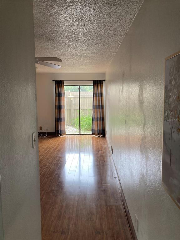 A narrow room with wood-look flooring, a popcorn ceiling, and sliding glass doors to a yard — 8014 PEACH DRIVE UNIT 99, TAMPA, FL