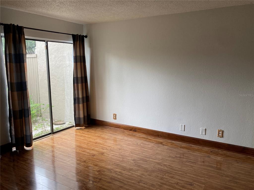 An empty room features wood-look flooring, beige walls, a sliding glass door, and brown curtains — 8014 PEACH DRIVE UNIT 99, TAMPA, FL
