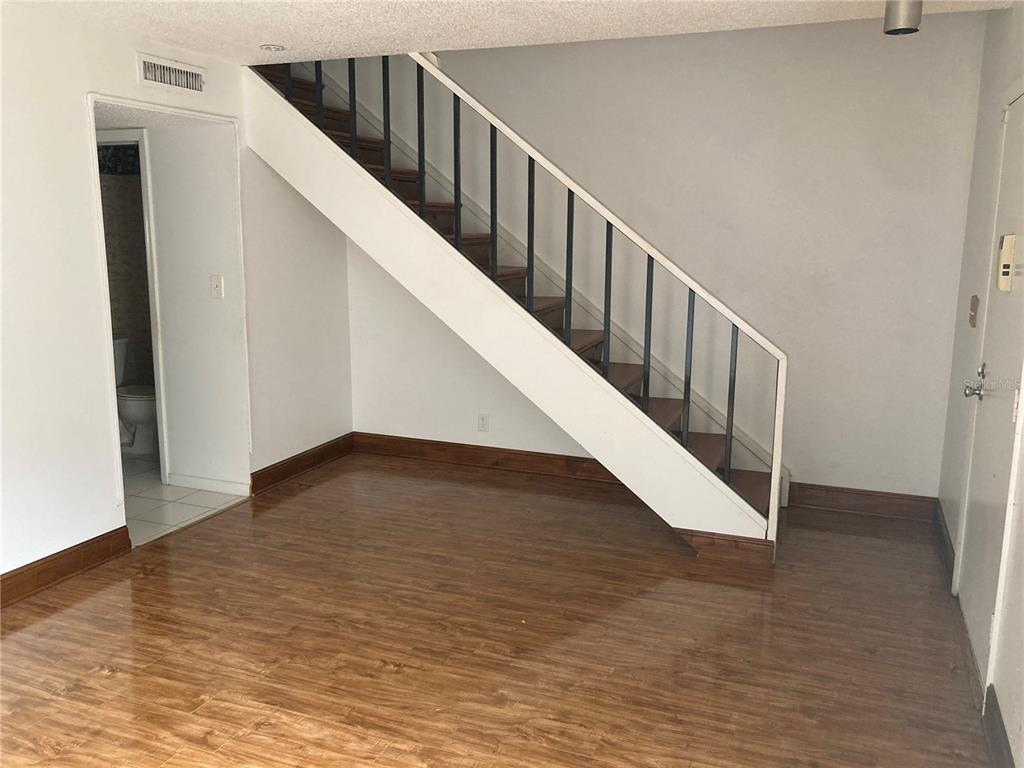 A room with wood-look flooring features a staircase with dark railings and a white frame — 8014 PEACH DRIVE UNIT 99, TAMPA, FL