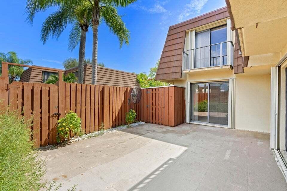 A concrete patio sits outside a two-story building with a wooden fence and palm tree — 3960 August Drive, Lake Worth FL 33461, LAKE WORTH, FL