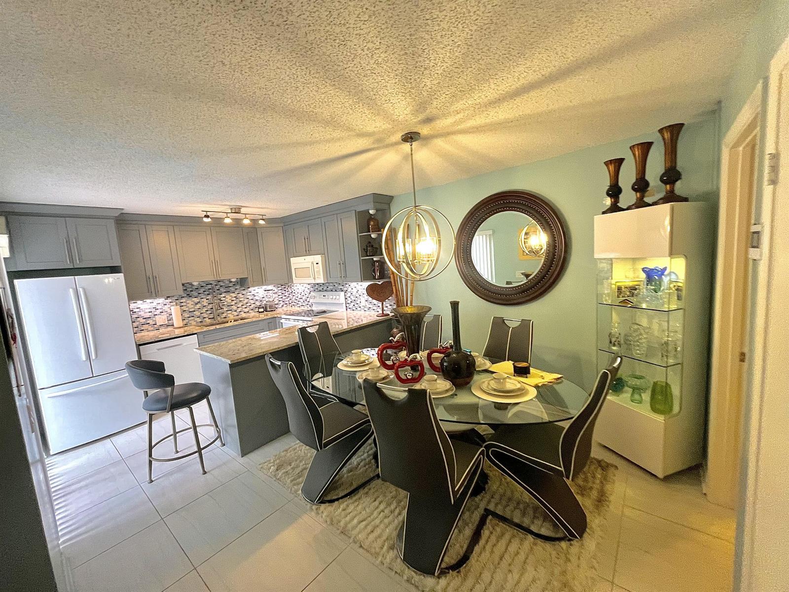 A dining area with a glass table and modern chairs sits adjacent to a gray kitchen — 3960 August Drive, Lake Worth FL 33461, LAKE WORTH, FL