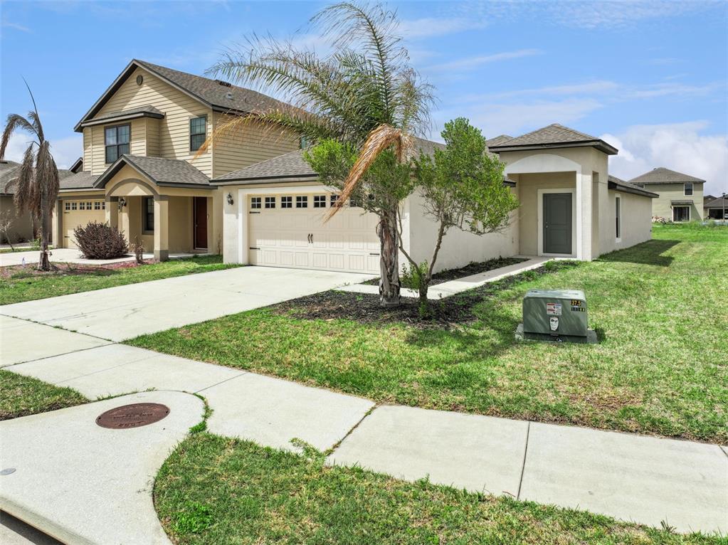 A tan, single-story house with a two-car garage and a palm tree in the yard — 2447 CASPIAN DRIVE, LAKELAND, FL