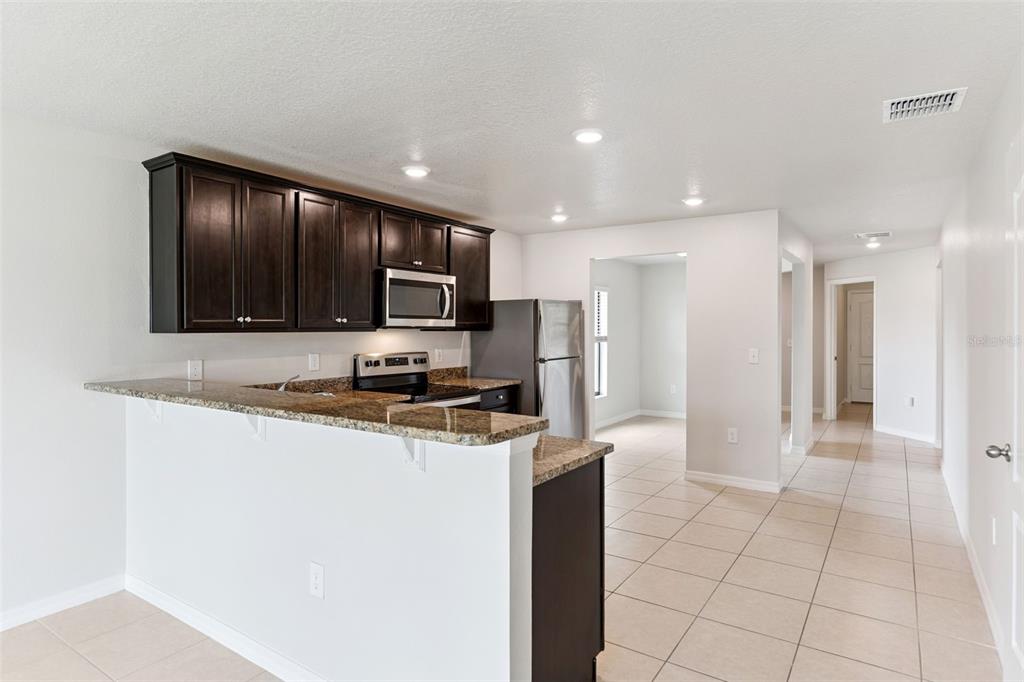 A kitchen with dark wood cabinets, granite countertops, stainless steel appliances, and tile flooring — 2447 CASPIAN DRIVE, LAKELAND, FL