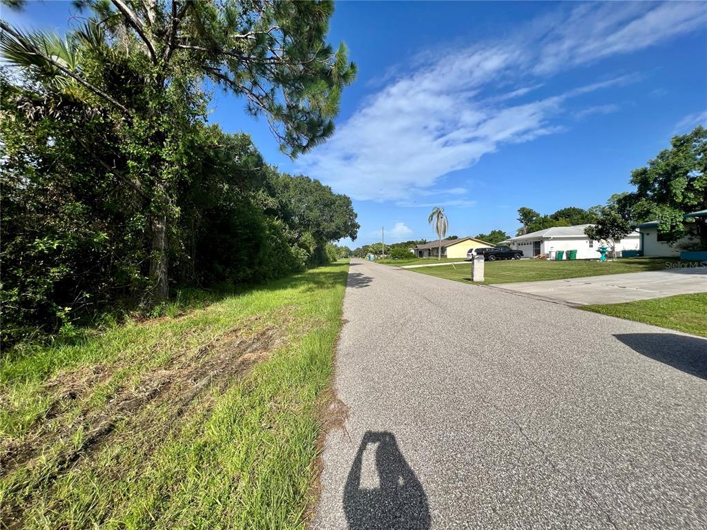 A paved residential street lined with trees and houses under a blue sky — 13544 DRYSDALE AVENUE, PORT CHARLOTTE, FL