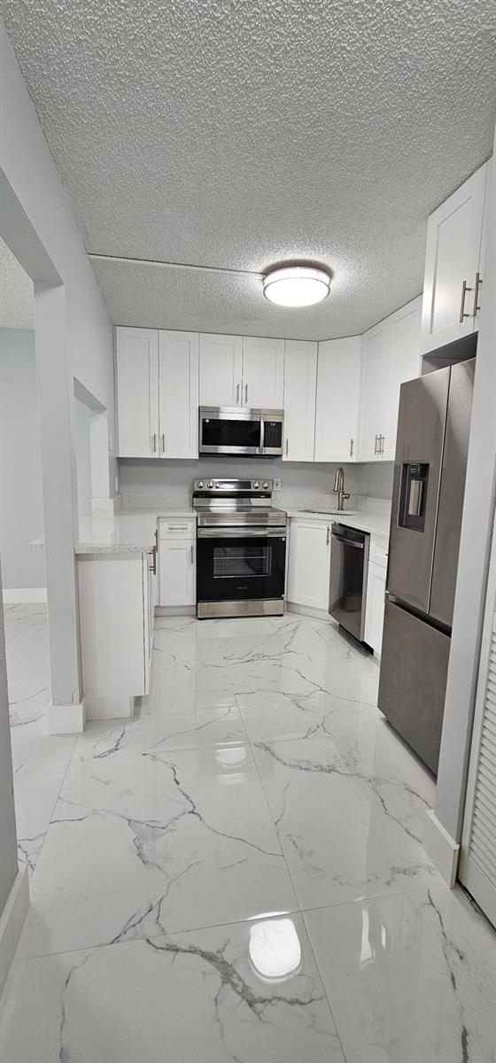 A modern kitchen features white cabinets, stainless steel appliances, and white marble-patterned tile flooring — 4991 Sable Pine Circle # B1, West Palm Beach FL 33417, WEST PALM BEACH, FL