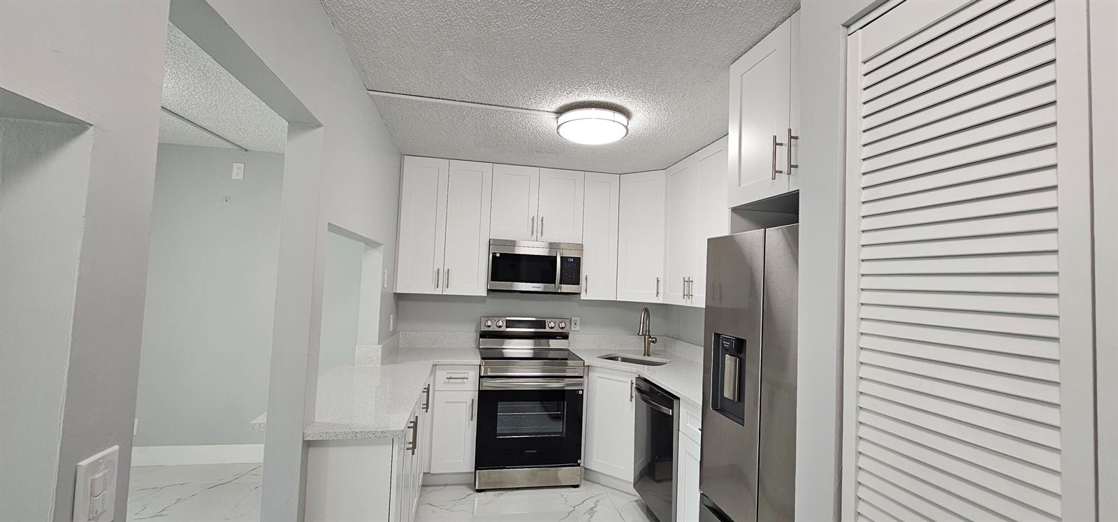 A kitchen features white cabinets, stainless steel appliances, quartz countertops, and white marble-look flooring — 4991 Sable Pine Circle # B1, West Palm Beach FL 33417, WEST PALM BEACH, FL