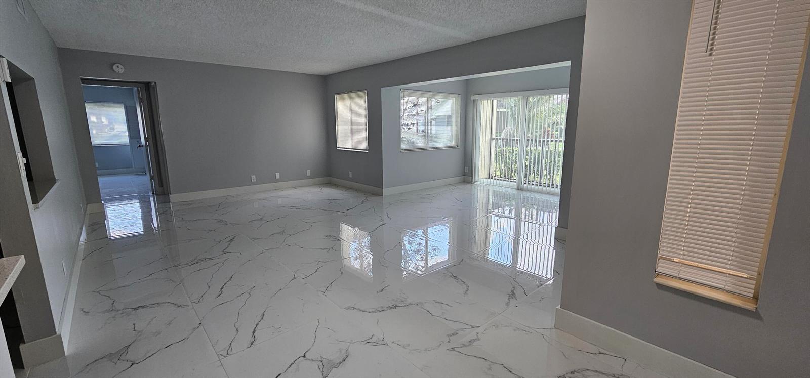 An empty living room features gray walls, white marble-look tile flooring, and large windows — 4991 Sable Pine Circle # B1, West Palm Beach FL 33417, WEST PALM BEACH, FL