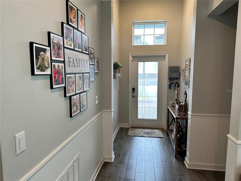 A bright entryway features a gallery wall, wood-look tile flooring, and a front door with glass — 556 BRUNSWICK DRIVE, DAVENPORT, FL