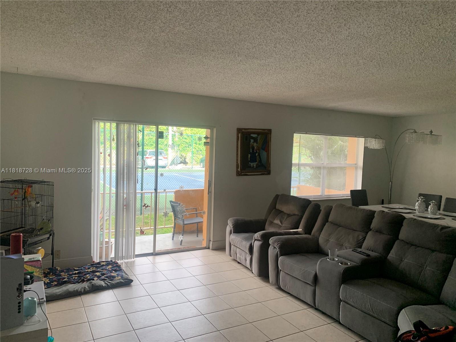 A living room with tiled floors, a gray sectional sofa, and a sliding glass door — 17911 NW 68th Ave # O104, Hialeah FL 33015, HIALEAH, FL