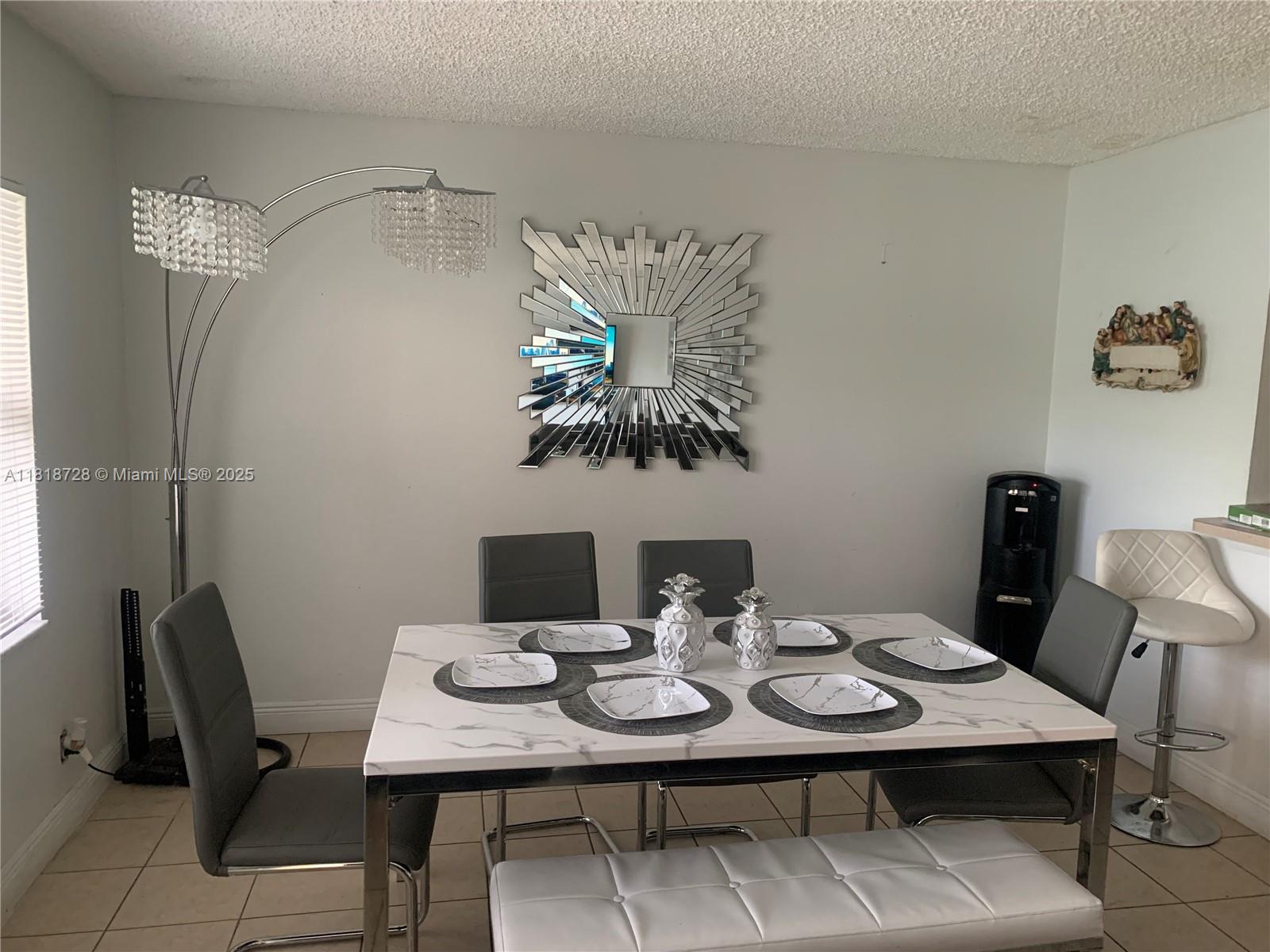 A dining room features a marble-top table, gray chairs, a white bench, and a sunburst mirror — 17911 NW 68th Ave # O104, Hialeah FL 33015, HIALEAH, FL