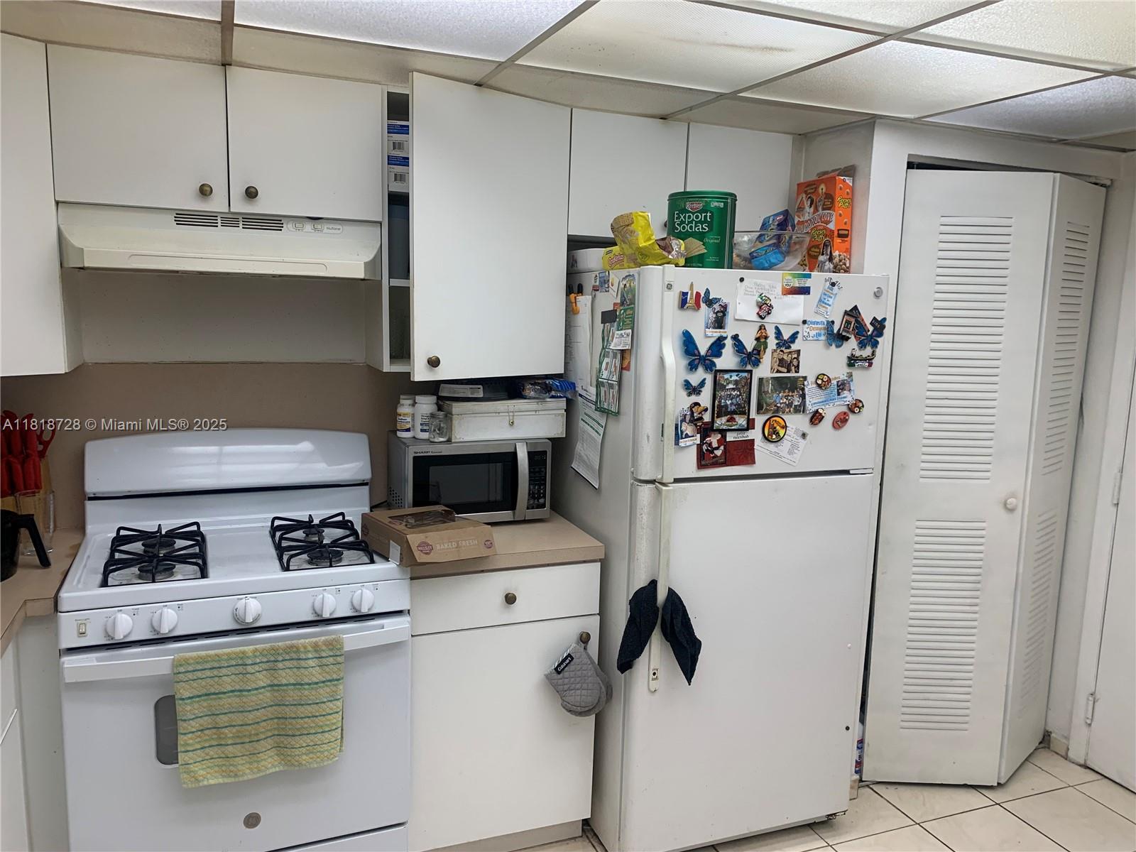 A kitchen features white cabinets, a white stove, a microwave, and a refrigerator with magnets — 17911 NW 68th Ave # O104, Hialeah FL 33015, HIALEAH, FL