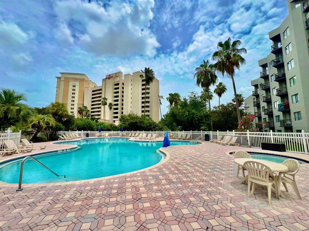 A swimming pool with a paved deck and lounge chairs sits before two large buildings — 6165 CARRIER DRIVE UNIT 3311, ORLANDO, FL