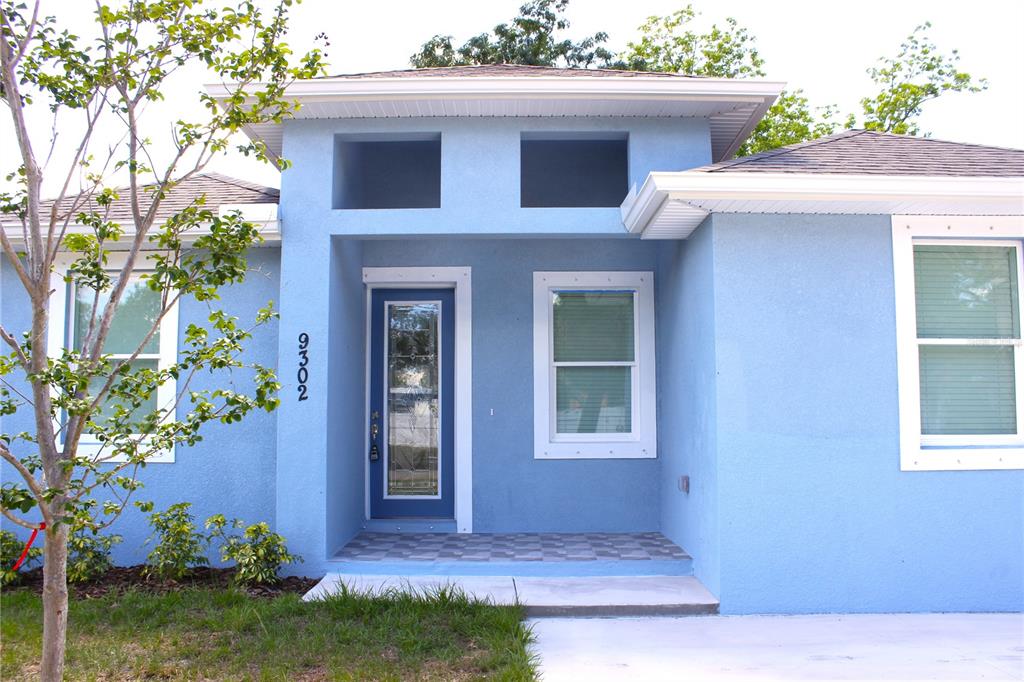 A light blue house exterior features a recessed front door and two rectangular transom windows — 9302 N 18TH STREET, TAMPA, FL