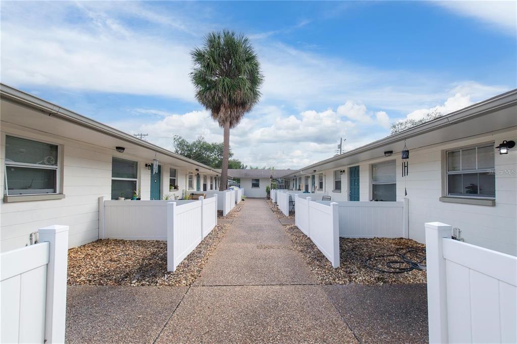 A concrete walkway leads between two rows of white single-story apartment units with fenced patios — 500 75TH AVENUE N, ST PETERSBURG, FL
