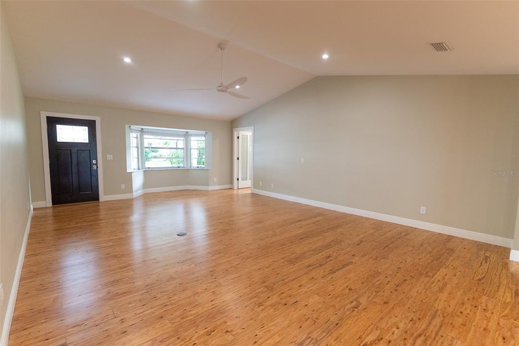 An empty living room features light wood flooring, a vaulted ceiling, and a bay window — 8743 SW 90TH LANE UNIT A, OCALA, FL