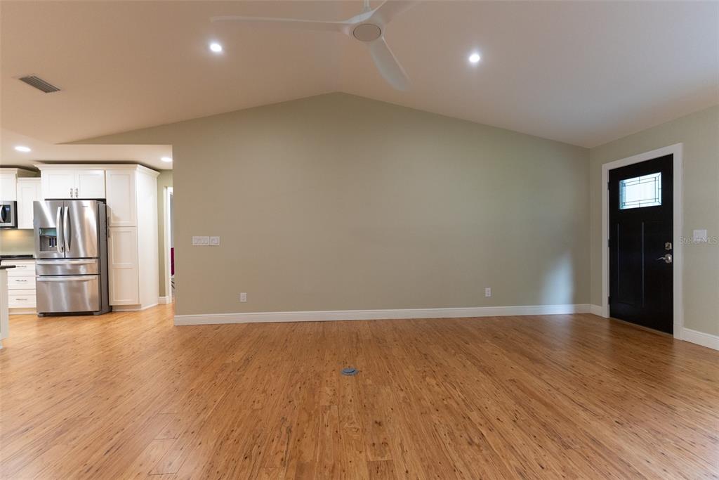 A spacious room with light green walls, wood flooring, a ceiling fan, and a black door — 8743 SW 90TH LANE UNIT A, OCALA, FL