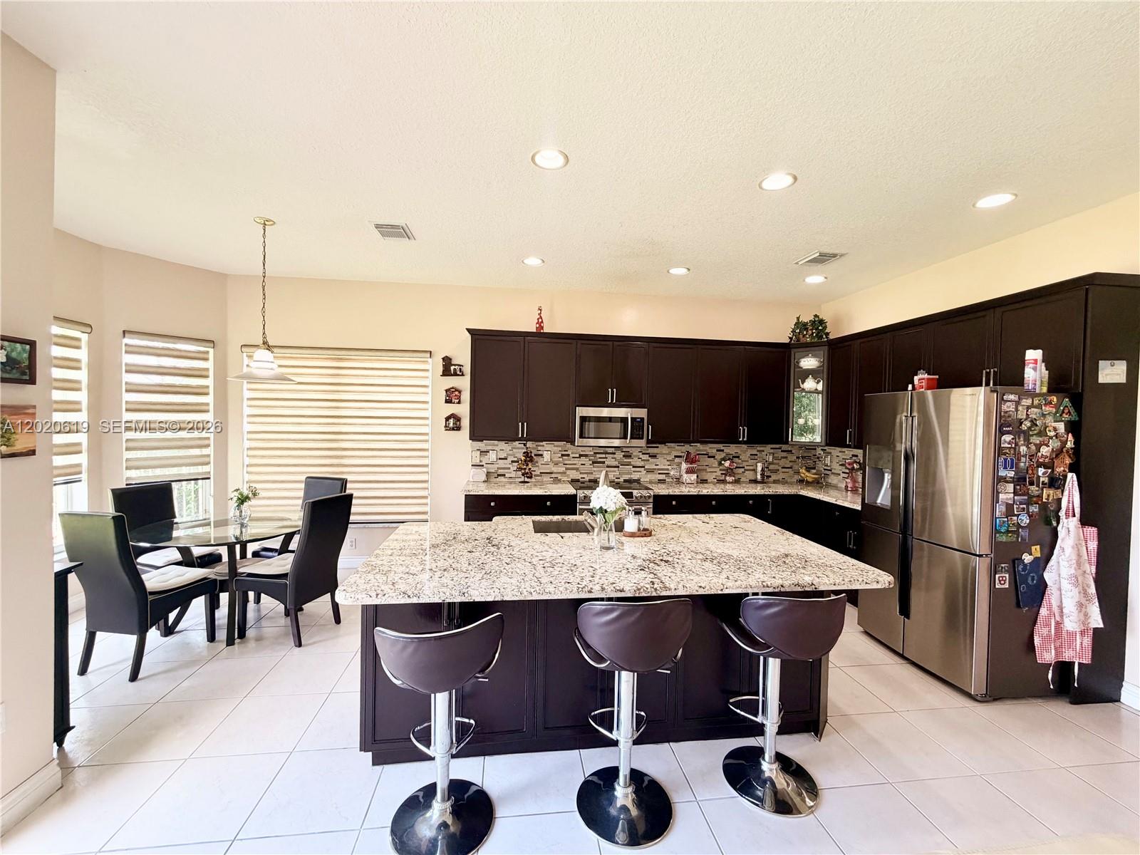 A kitchen features dark wood cabinets, granite countertops, a central island, and a dining area — 18815 SW 29th St, Miramar FL 33029, MIRAMAR, FL