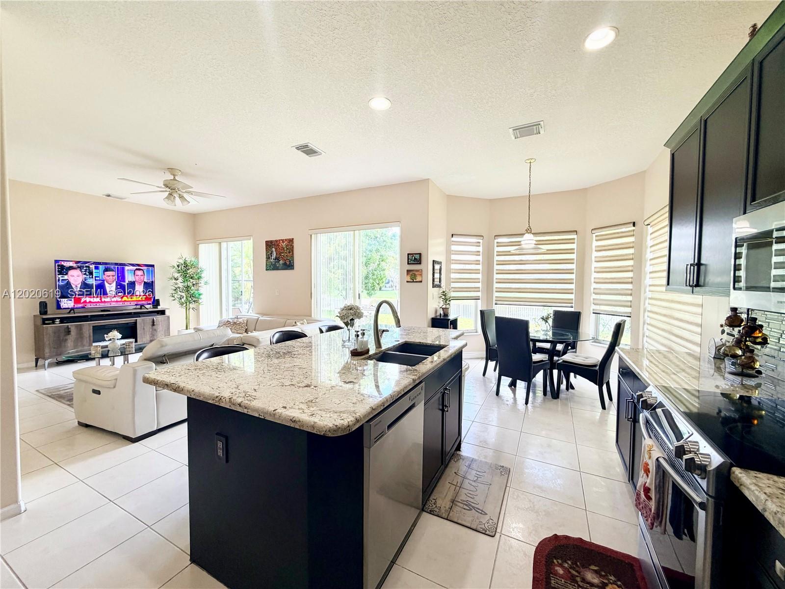 An open-concept kitchen with a granite island, dark cabinetry, and tile flooring overlooks a living area — 18815 SW 29th St, Miramar FL 33029, MIRAMAR, FL