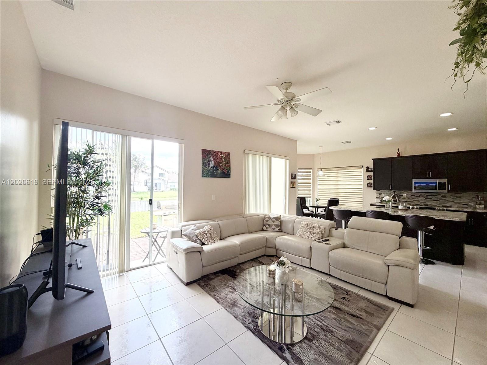 A living room with a white sectional sofa, glass coffee table, and an open kitchen — 18815 SW 29th St, Miramar FL 33029, MIRAMAR, FL