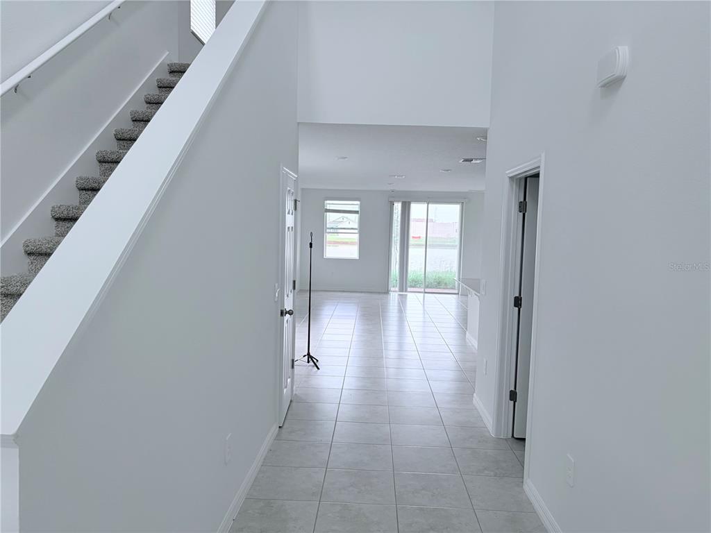 A bright entryway features a carpeted staircase, tile flooring, and a view toward the backyard — 3213 VICEROY COURT, POINCIANA, FL