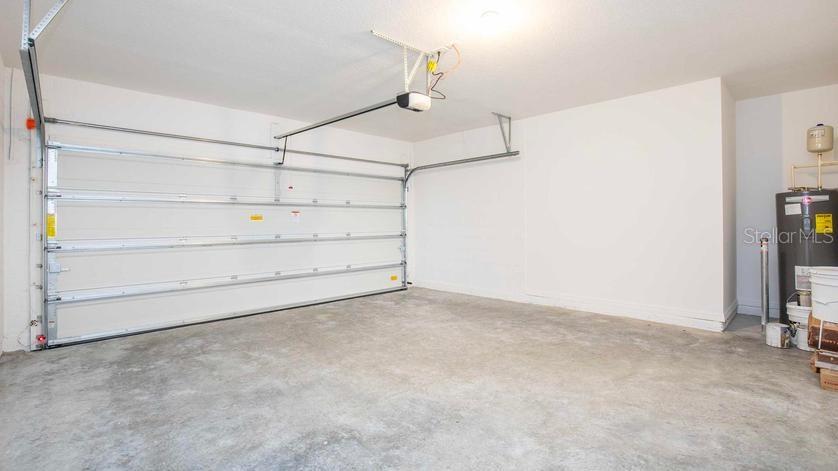 An empty garage features a concrete floor, a white sectional door, and a water heater — 3213 VICEROY COURT, POINCIANA, FL