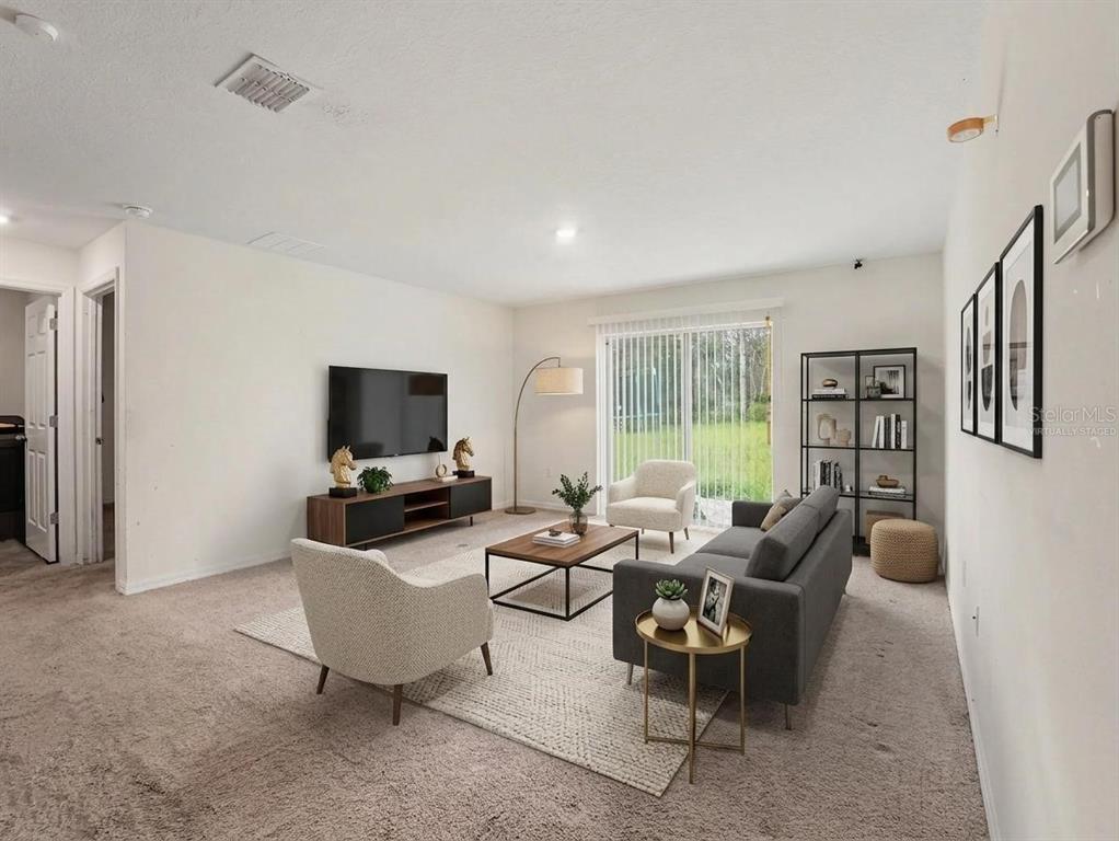 A living room with carpeted floors, a gray sofa, two armchairs, and a television — 305 BOWFIN DRIVE, KISSIMMEE, FL