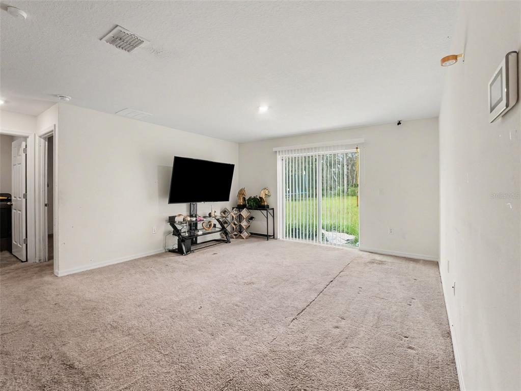 A carpeted living room features a television on a stand and sliding glass patio doors — 305 BOWFIN DRIVE, KISSIMMEE, FL