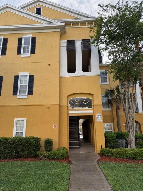 A three-story yellow apartment building features a central recessed entryway and a paved walkway — 3707 CONROY ROAD UNIT 1712, ORLANDO, FL