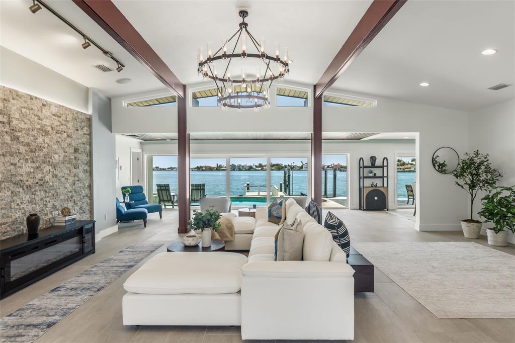 A modern living room features a stone fireplace, white sectional sofa, and floor-to-ceiling water views — 4598 CLEARWATER HARBOR DRIVE S, LARGO, FL
