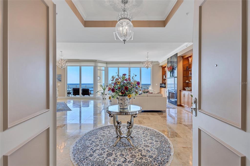 A foyer with a circular rug and pedestal table opens into a bright, marble-floored living area — 130 RIVIERA DUNES WAY UNIT PH202, PALMETTO, FL