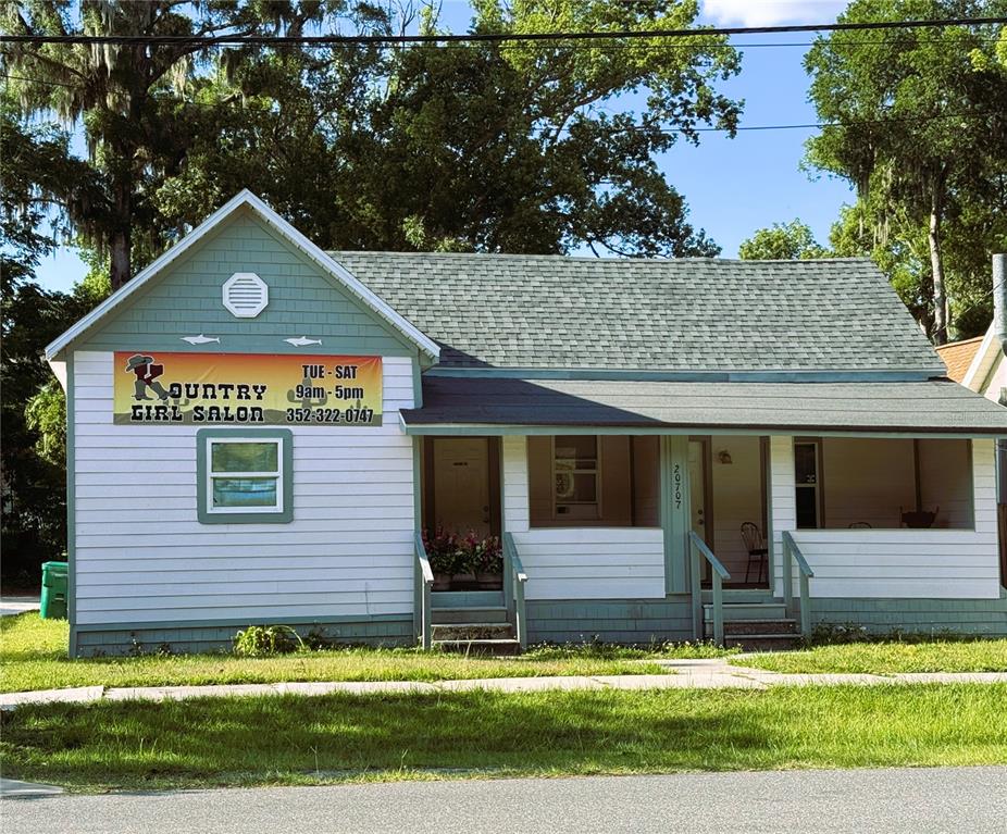 A single-story building with white siding and a green roof serves as a hair salon — 20707 WALNUT STREET, DUNNELLON, FL