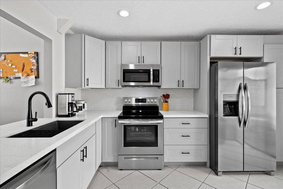 A modern kitchen features light gray cabinets, stainless steel appliances, and white countertops — 12875 Spinnaker Lane, Wellington FL 33414, WELLINGTON, FL