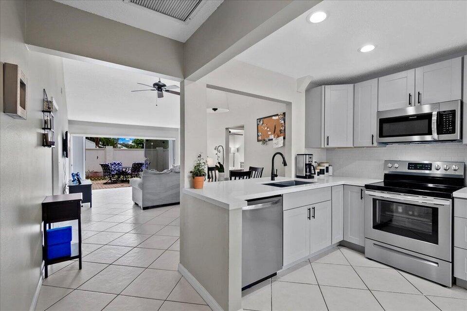 A kitchen with white cabinets and stainless steel appliances opens to a tiled living area — 12875 Spinnaker Lane, Wellington FL 33414, WELLINGTON, FL