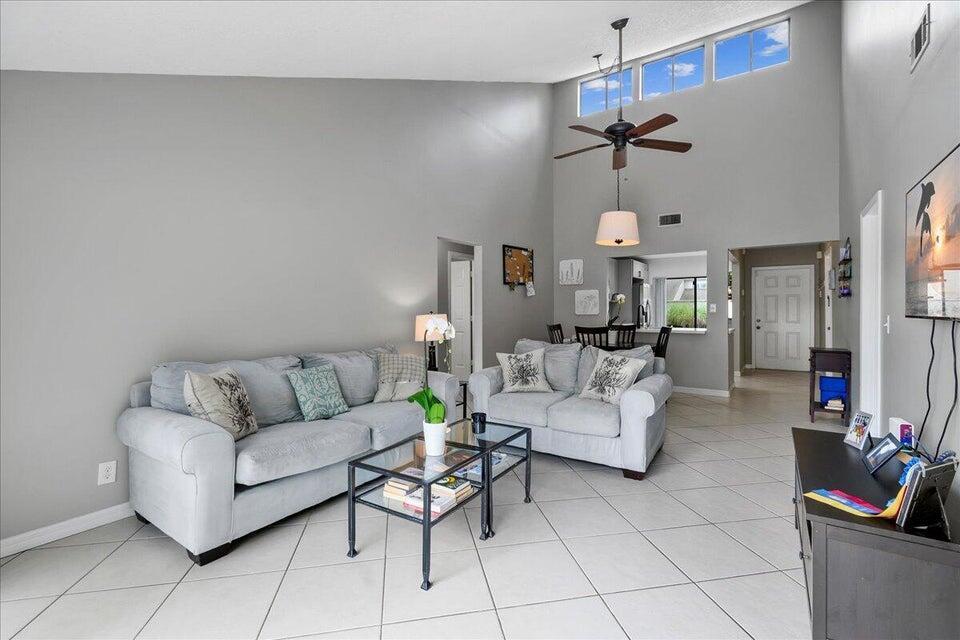 A living room with vaulted ceilings, tile floors, two gray sofas, and a glass coffee table — 12875 Spinnaker Lane, Wellington FL 33414, WELLINGTON, FL