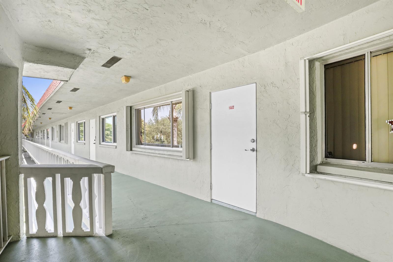An exterior walkway with white walls, a white door, and windows overlooking a palm tree — 3100 Springdale Boulevard # 308, Palm Springs FL 33461, PALM SPRINGS, FL