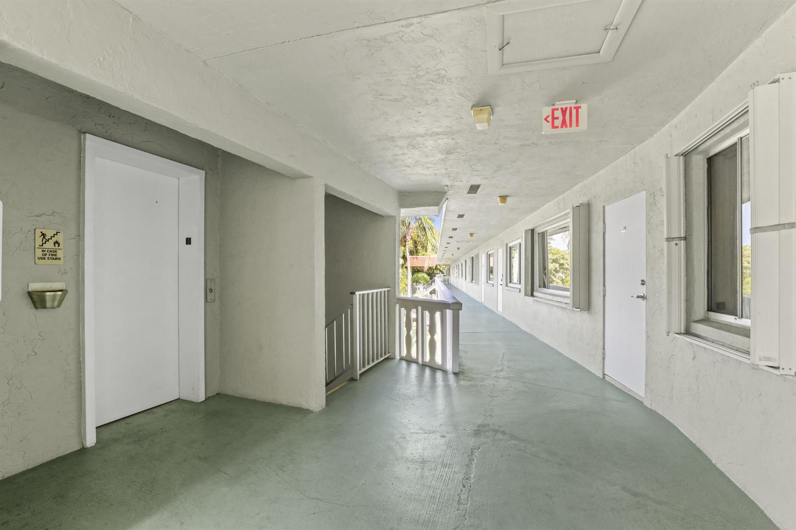 An outdoor apartment building walkway features white doors, a staircase, and a green floor — 3100 Springdale Boulevard # 308, Palm Springs FL 33461, PALM SPRINGS, FL